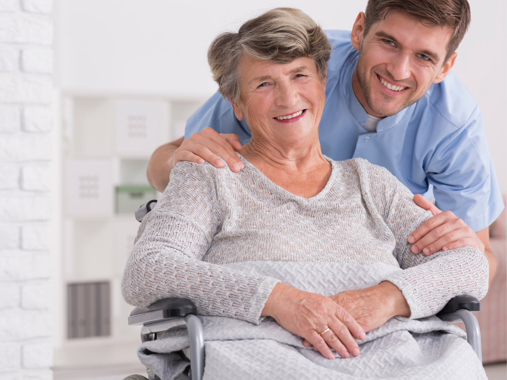 Smiling elderly woman in a wheelchair with a caregiver standing behind her, both looking happy. Senior home care in Falmouth