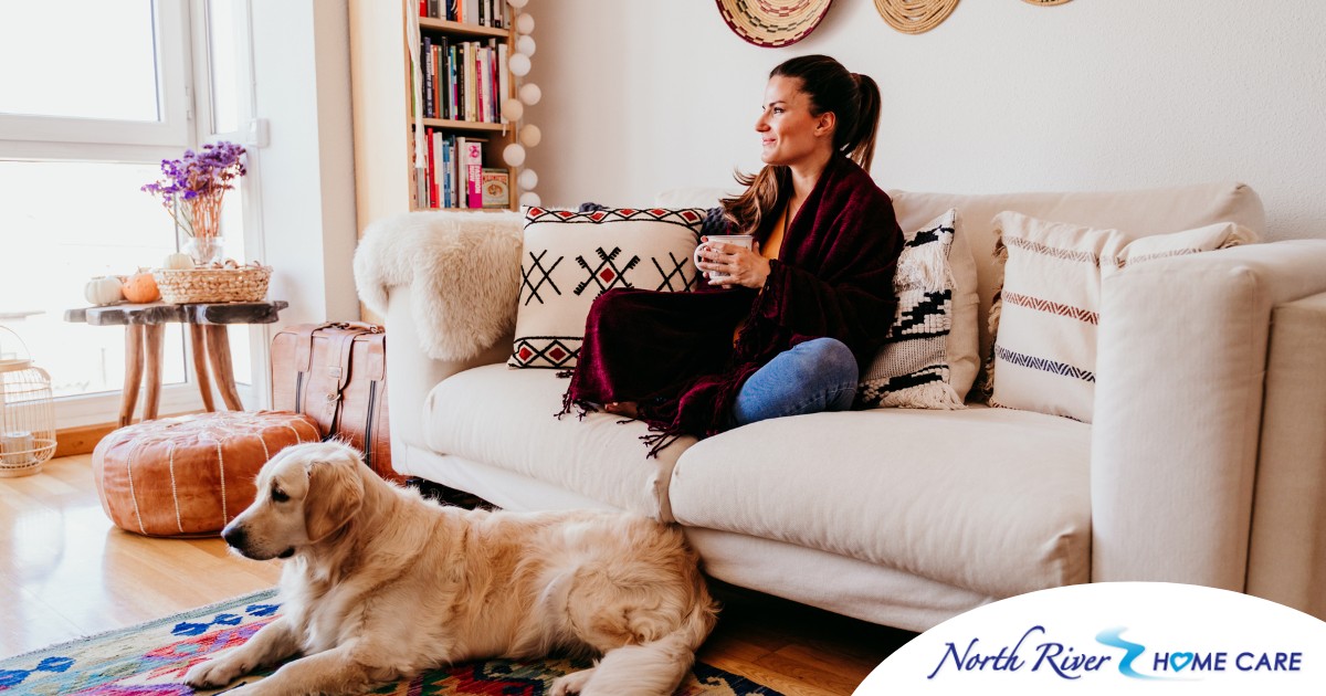 A woman relaxes with her dog while sipping on tea, representing how self-care can combat caregiver stress.