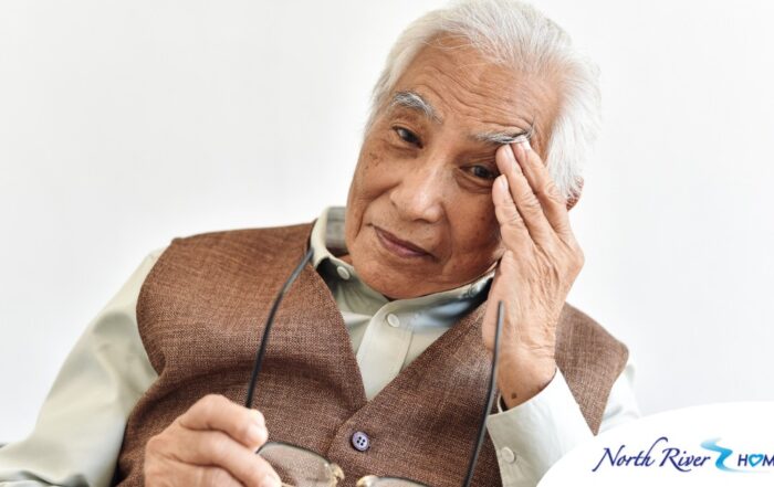 An older adult holds his head and his glasses representing vision problems like macular degeneration.
