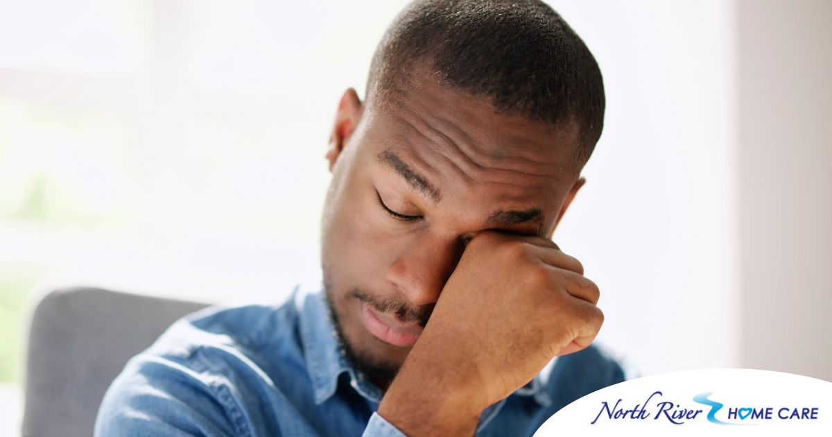 A man tiredly rubs his eyes, representing the exhaustion that can come with family caregiving.